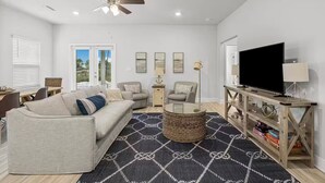 A living room with a sofa, armchairs, a coffee table, a TV, and a bookshelf. - Golf Cart • EV Charger • Pool • Walk to Beach • 2 Kitchens • Private Suite (Port St. Joe)
