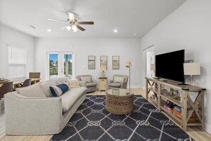 A living room with a sofa, armchairs, a coffee table, a TV, and a bookshelf. - Golf Cart • EV Charger • Pool • Walk to Beach • 2 Kitchens • Private Suite (Port St. Joe)