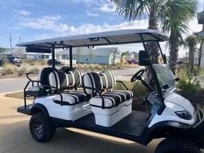 A golf cart parked in a residential area with houses in the background. - Golf Cart • EV Charger • Pool • Walk to Beach • 2 Kitchens • Private Suite (Port St. Joe)