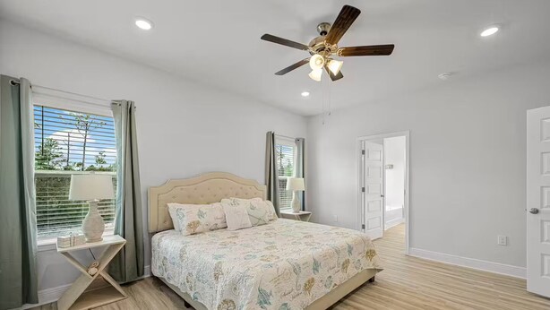 A bedroom with a bed, bedside tables, a ceiling fan, and a window with curtains. - Golf Cart  • EV Charger • Pool • Walk to Beach • 2 Kitchens • Private Suite (Port St. Joe)