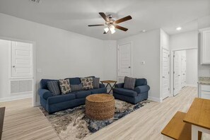 A living room with a sectional sofa, a ceiling fan, and a small table. - Golf Cart • EV Charger • Pool • Walk to Beach • 2 Kitchens • Private Suite (Port St. Joe)