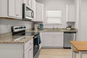 A modern kitchen with white cabinetry, a built-in oven, a dishwasher, and a window with blinds. - Golf Cart • EV Charger • Pool • Walk to Beach • 2 Kitchens • Private Suite (Port St. Joe)