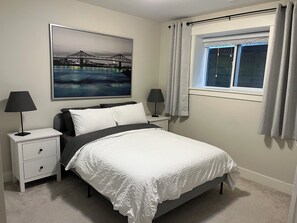 Ein Schlafzimmer mit einem Bett, zwei Nachttischen, einem Fenster mit Vorhängen und einem Stadtbild an der Wand.