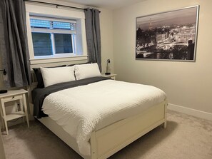 Une chambre à coucher avec un lit, une table de chevet, une fenêtre avec des rideaux et une affiche représentant un paysage urbain accrochée au mur.