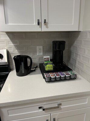 Un comptoir de cuisine avec une machine à café, une bouilloire et un plateau de dosettes de café.