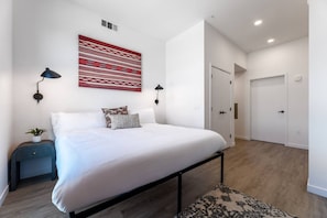 Un dormitorio moderno con una cama grande, lámparas de noche, una obra de arte en la pared y una puerta que da a otra habitación.