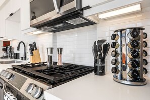 A modern kitchen with a gas stove, stainless steel appliances, and a spice rack.