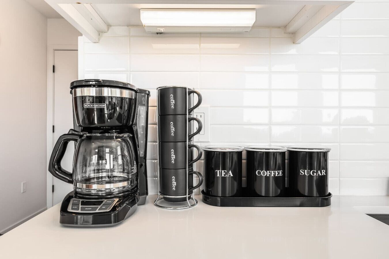 A kitchen with a coffee maker, four coffee mugs, and a tea container.