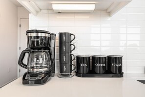 A kitchen with a coffee maker, four coffee mugs, and a tea container.