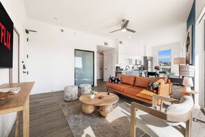 Een moderne woonkamer met een bank, voetenbankjes, een salontafel en een eethoek.