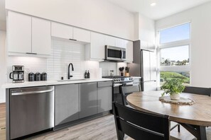 Una cocina moderna con electrodomésticos de acero inoxidable, armarios blancos y vistas a un paisaje verde a través de un ventanal amplio.
