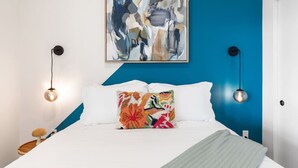 A modern bedroom with a bed, a colorful abstract painting, and two wall-mounted lamps. - Modern DTLA Apartment Minutes from Dodger Stadium (Los Angeles)