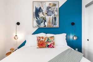 A modern bedroom with a bed, a colorful abstract painting, and two wall-mounted lamps.