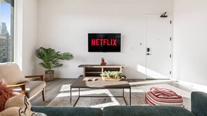 A modern living room with a flat-screen TV mounted on the wall, a coffee table, a sofa, and a door. - Modern DTLA Apartment Minutes from Dodger Stadium (Los Angeles)