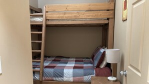 Ein Etagenbett mit kariertem Bettbezug und Kissen, ein Nachttisch mit Lampe sowie eine Tür rechts.