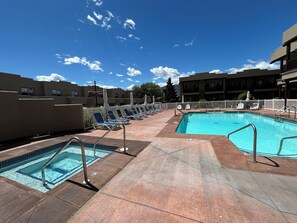 Un espace piscine comprenant plusieurs bassins, des chaises longues et un ciel dégagé.