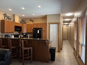A kitchen with wooden cabinets, a black refrigerator, a microwave, and a granite countertop.