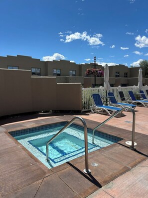 A pool area with a tiled pool, lounge chairs, and a white fence.