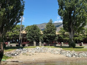 Un bâtiment doté d’une façade en pierre, une zone pavée bordée d’un muret en pierre, et une vue sur les montagnes en arrière-plan.