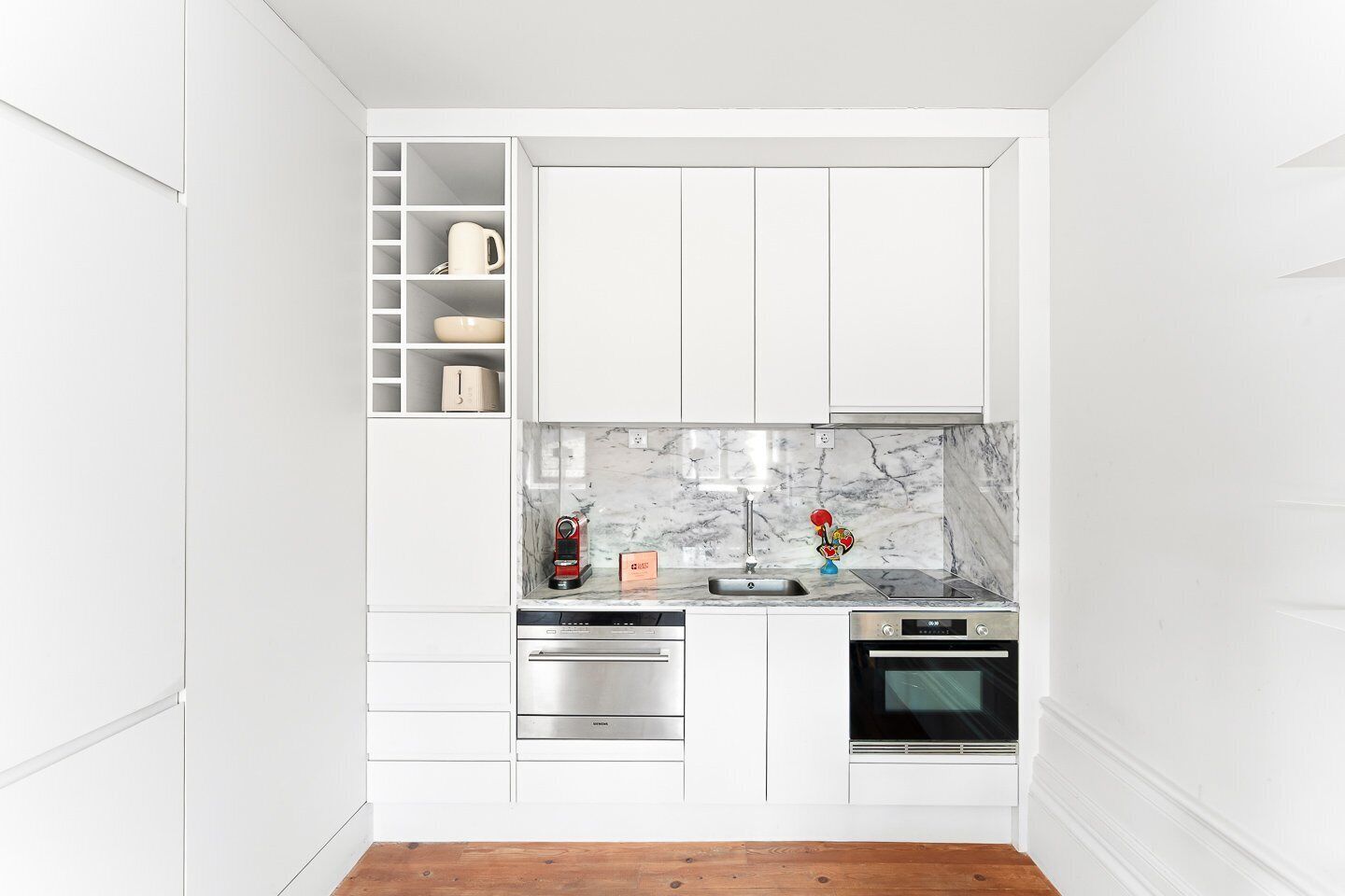 A compact kitchen with white cabinetry, a marble backsplash, and stainless steel appliances.