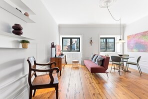 A modern living room with a wooden floor, a red sofa, a dining table with chairs, and a large window with a view. - GuestReady - Porto Charming Retreat (Porto)