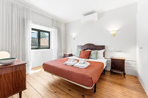 Hotelkamer met houten vloer, een bed met een rood-wit stippen dekbed, een houten nachtkastje, een bijzettafeltje met een lamp en een raam met gordijnen.