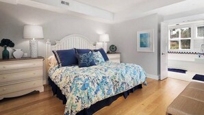 A bedroom with a bed, bedside tables, a nightstand, a lamp, a picture on the wall, and a door leading to a balcony. - Lakefront Luxury Retreat - Beach & Mountain Views  (Kelowna)