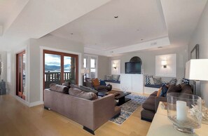Ein geräumiges Wohnzimmer mit einer großen Couch, einem Couchtisch und einem Fernseher. Ein Balkon bietet Blick auf die Berge.