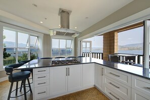 Eine moderne Küche mit einer zentralen Kochinsel, weißen Schränken und großen Fenstern mit Blick aufs Meer.