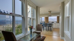 A modern interior with a dining area, kitchen, and large windows offering a view of the landscape. - Lakefront Luxury Retreat - Beach & Mountain Views  (Kelowna)