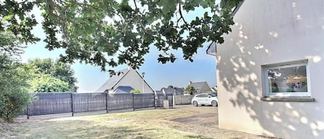 Ein Wohngebiet mit einem weißen Gebäude, einem eingezäunten Garten und einem geparkten Auto im Hintergrund.