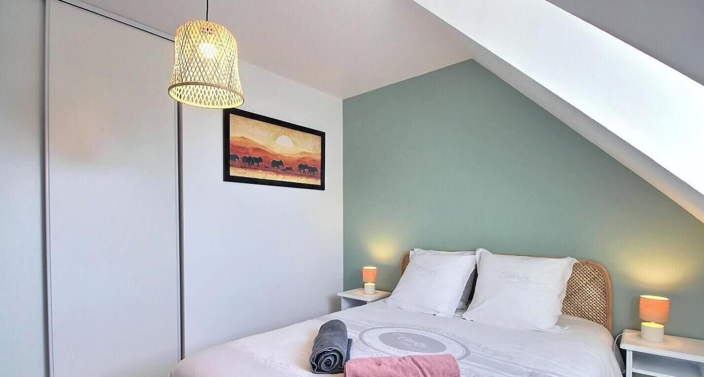 A bedroom with a bed, a hanging lamp, a painting, and a nightstand with a lamp.