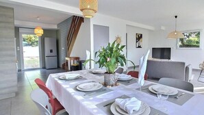 A dining area with a long table set for a meal, a potted plant, and a television in the background. - Ty Maezou - LANNION - Vacation Rental (LANNION)
