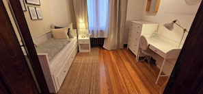Ein kleines Schlafzimmer mit Bett, Nachttisch, Lampe, Kommode und Schreibtisch.