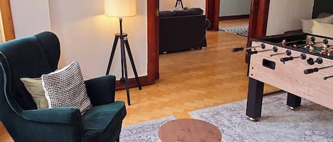 A living room with two green sofas, a round coffee table, a foosball table, and a lamp.