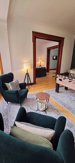 Ein Wohnzimmer mit zwei grünen Sofas, einem runden Couchtisch, einem Kicker und einer Lampe.