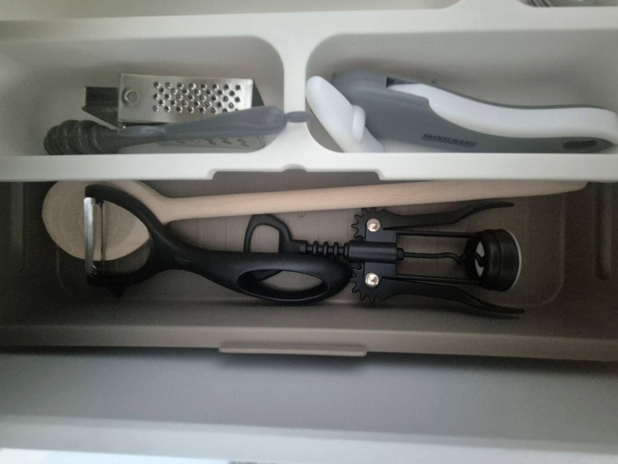 Uma gaveta com um ralador, uma escova de dentes, uma escova de cabelo e um cabo preto.