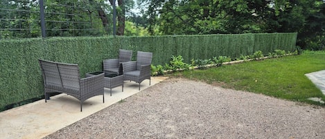 A gravel patio with a hedge and outdoor furniture.