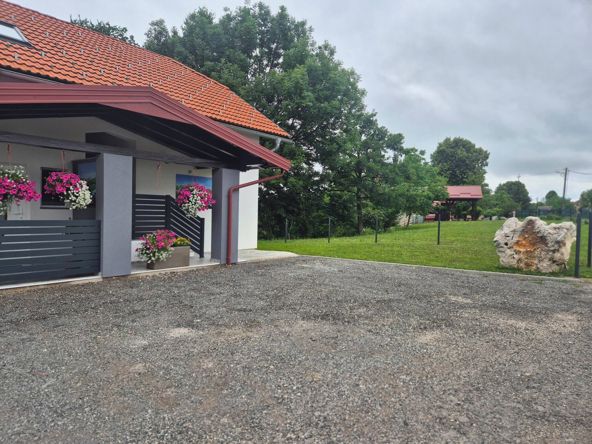 A building with a red-tiled roof, a gravel driveway, and a stone feature in the foreground.
