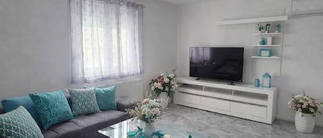 A modern living room with a grey sofa set, a glass coffee table, a flat-screen TV, and a white entertainment unit.