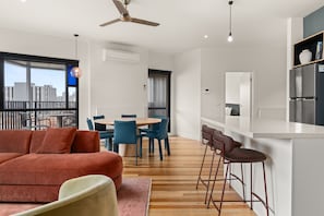 A modern living space with a sofa, dining area, kitchen, and a balcony with a city view. - Hawke & Hide Designer 3BR Balcony Retreat (West Melbourne)