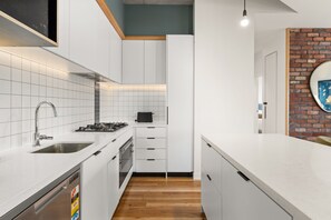 A modern kitchen with white cabinetry, a stainless steel sink, a gas stove, and a wooden floor. - Hawke & Hide Designer 3BR Balcony Retreat (West Melbourne)