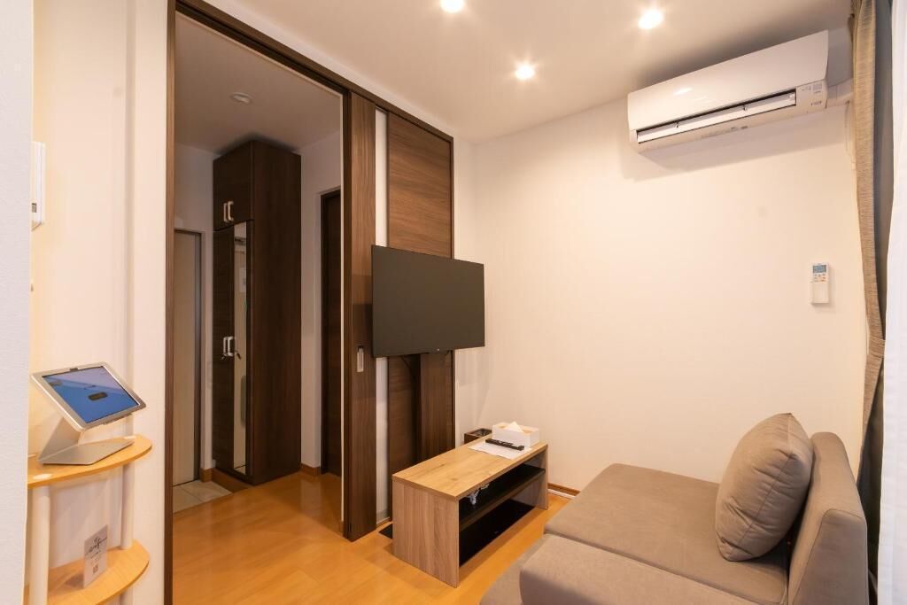 A modern hotel room with a flat-screen TV, a wooden entertainment unit, a sofa, and an air conditioning unit.