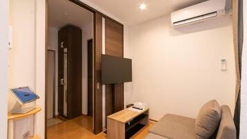 A modern hotel room with a flat-screen TV, a wooden entertainment unit, a sofa, and an air conditioning unit.
