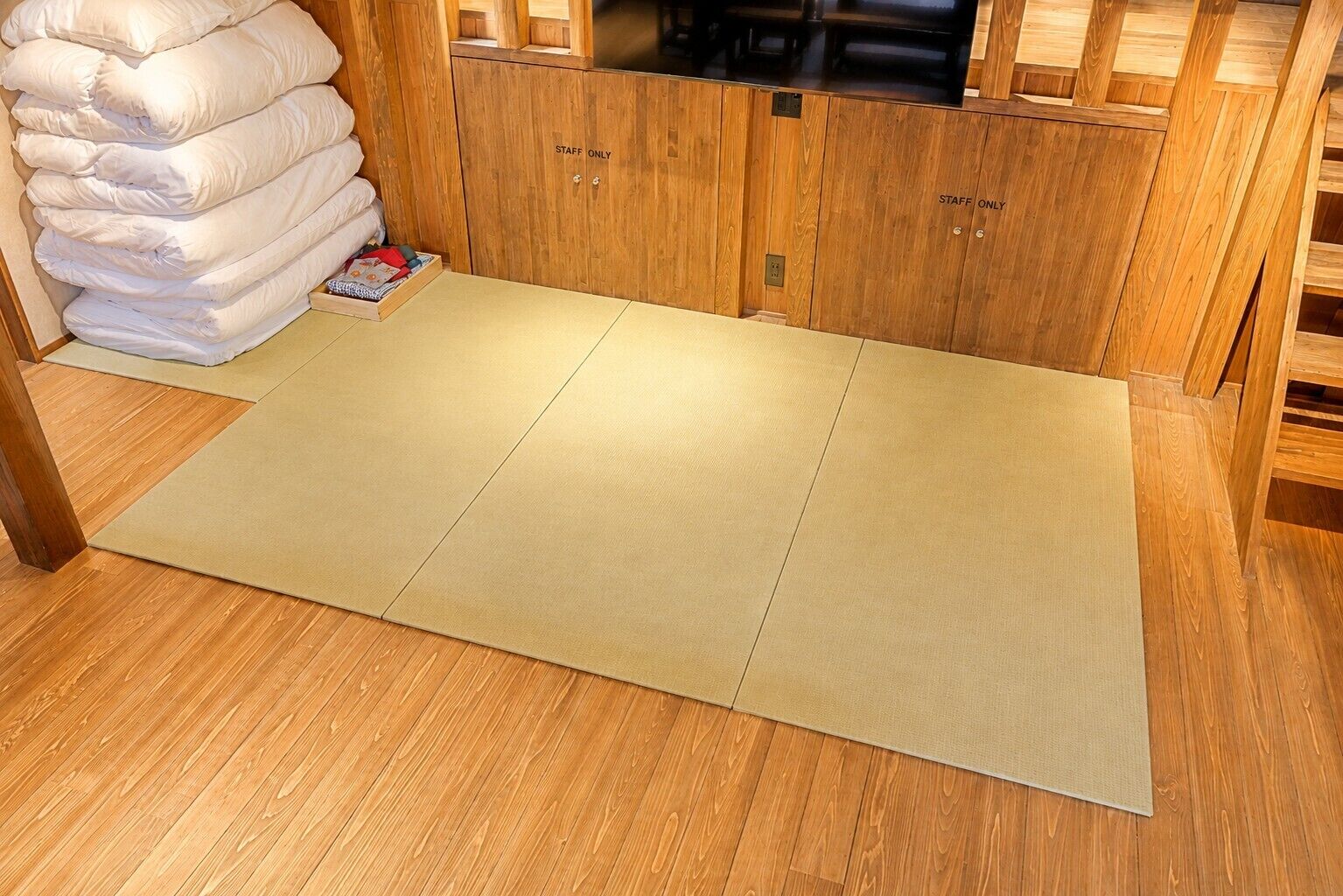 A room with a tatami mat floor, wooden cabinets, and a stack of white pillows.