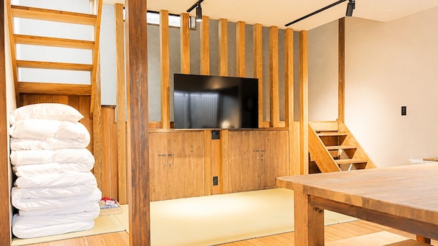 Un interno moderno con una scala in legno, una TV a schermo piatto montata su un mobile in legno e una pila di cuscini bianchi.