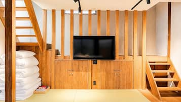 A room with a TV mounted on a wooden cabinet, a tatami mat floor, and a staircase.