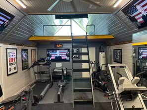 A gym with treadmills, weight machines, and a TV screen displaying an American flag. - Spacious 4 BR Retreat w/Fitness Center & Golf Simulator (Dallas)
