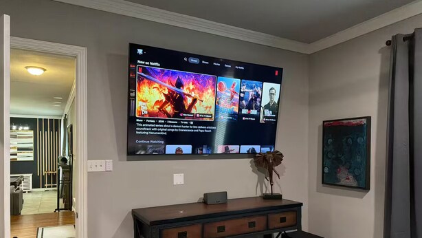 Ein Wohnzimmer mit einem an der Wand montierten Flachbildfernseher, der eine Netflix-Oberfläche anzeigt.