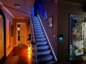 A staircase with blue LED lighting, a hallway with a wooden floor, and a wall with framed pictures. - Spacious 4 BR Retreat w/Fitness Center & Golf Simulator (Dallas)